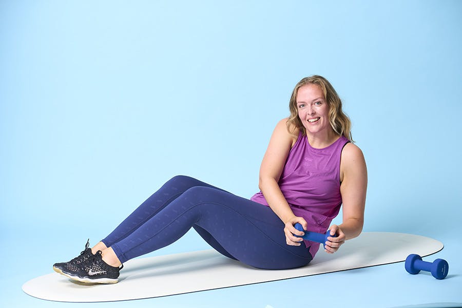 Leende kvinna på träningsmatta med vikter