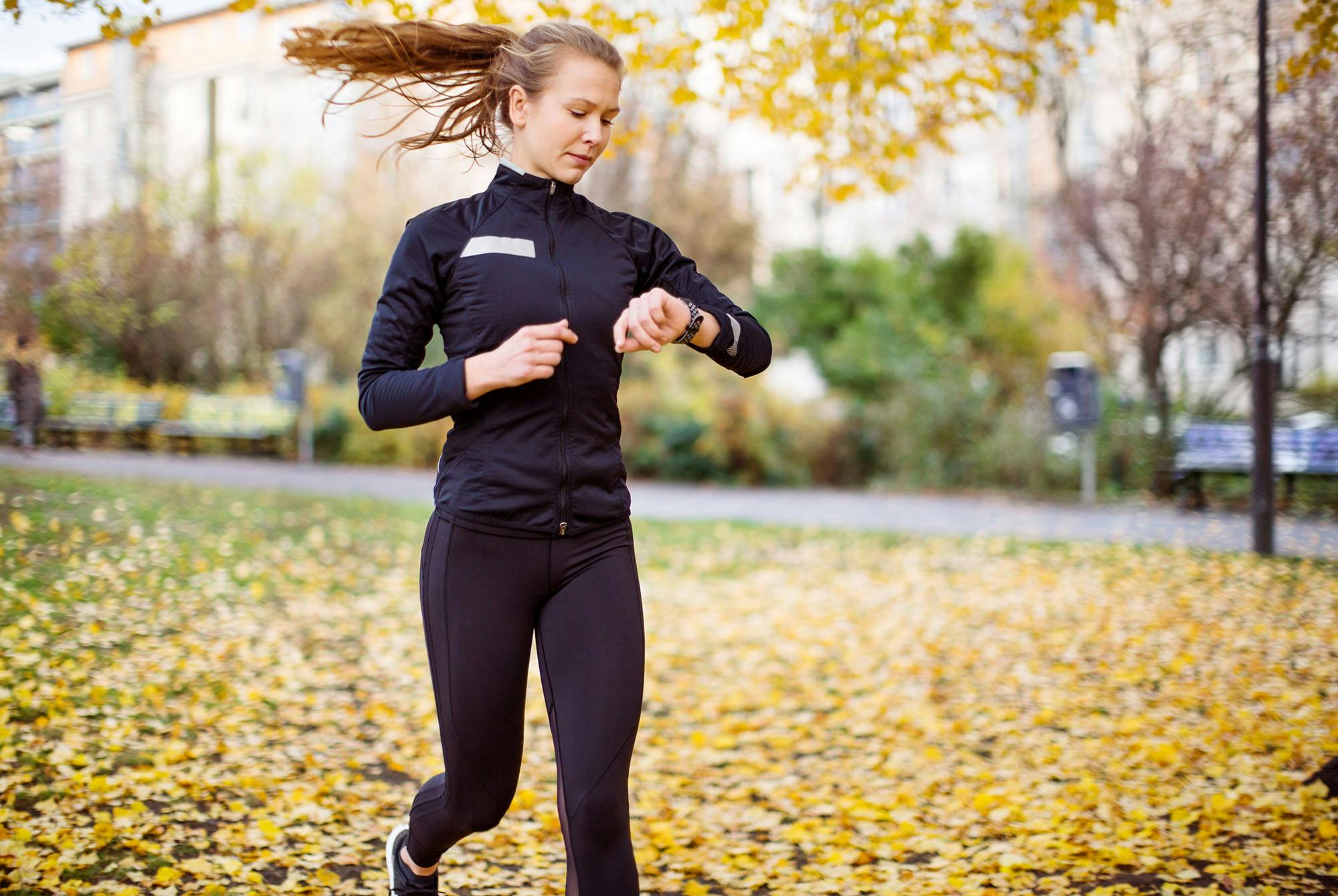 Kvinna som springer utomhus och tittar på sin klocka - vad är en bra 5 km-tid för löpning