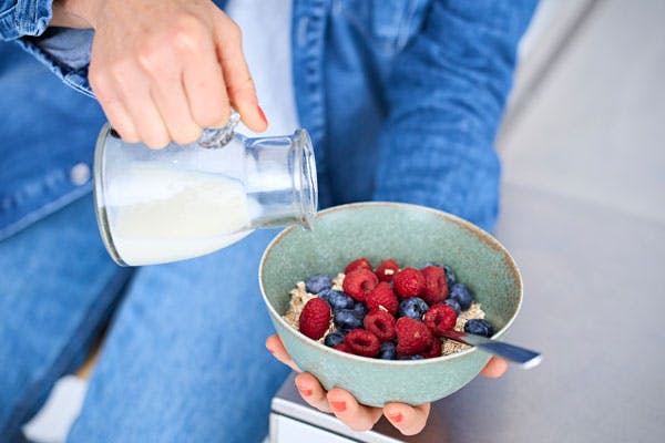 Kvinna häller mjölk på havregrynsgröt med massor av bär