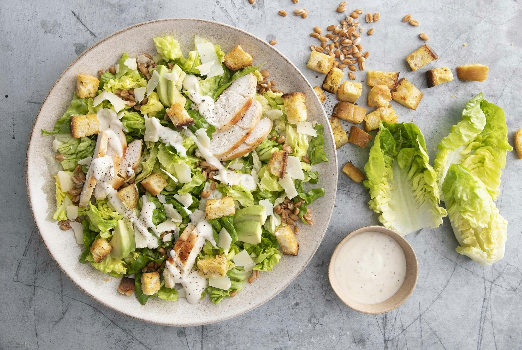 En tallerken Cæsarsalat med kylling, avocado, brødcroutoner og dressing.