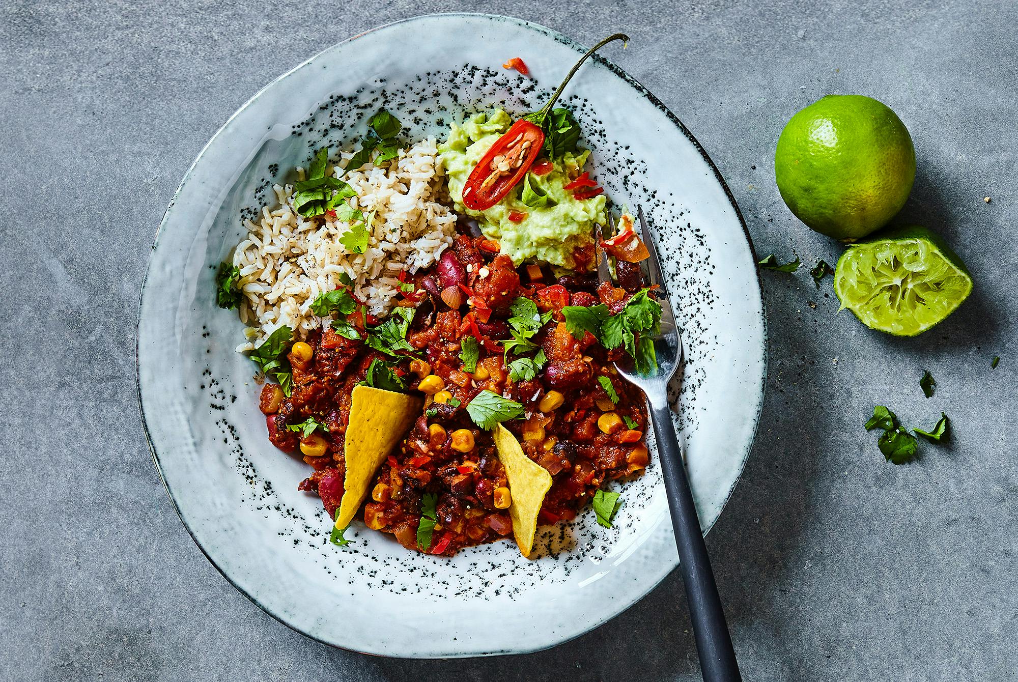 En tallerken chili sin carne med brune ris, avocadocreme og tortillachips.