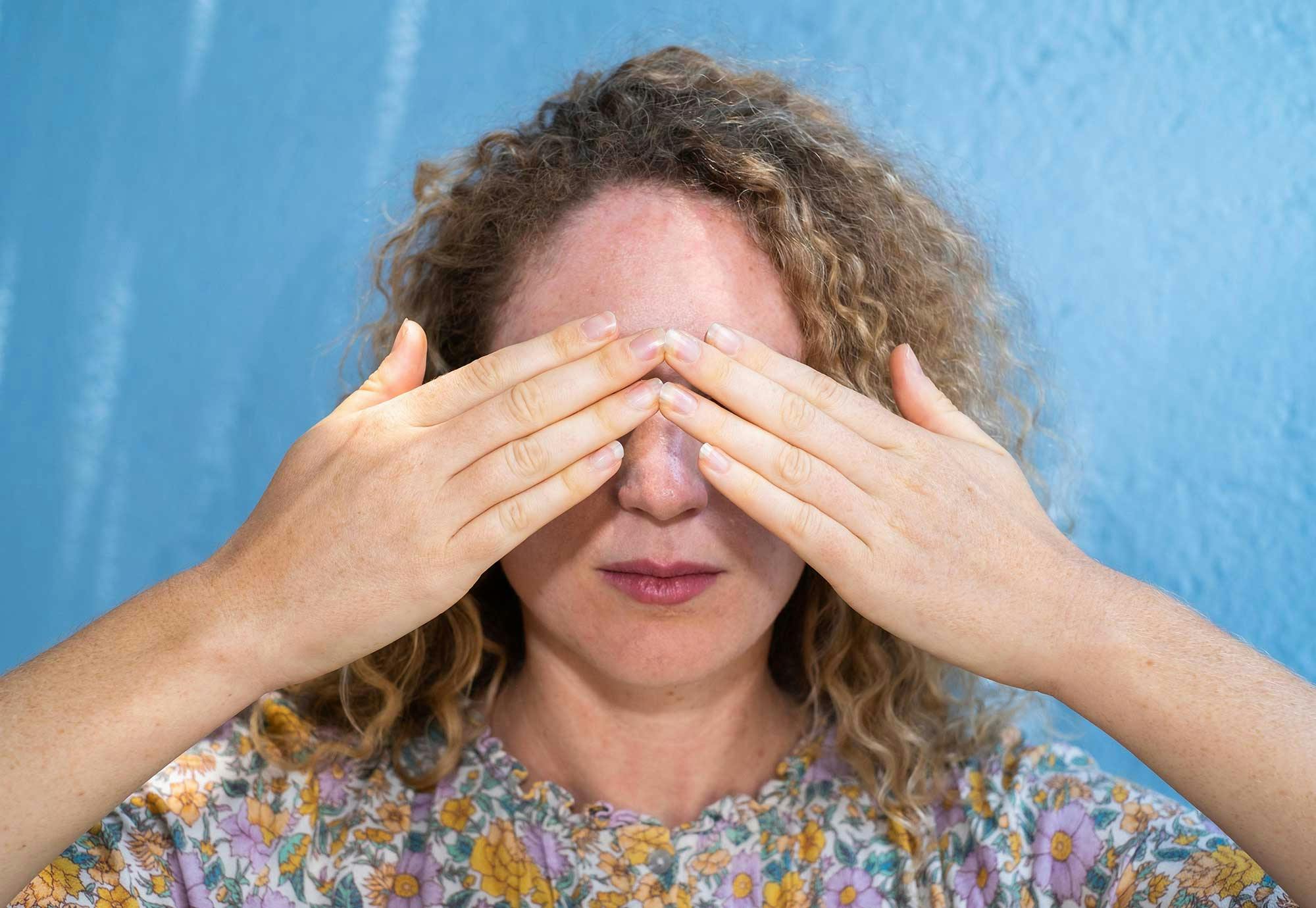 En kvinna håller för ögonen. Hon är färgblind och ser inte tecken på cancer.