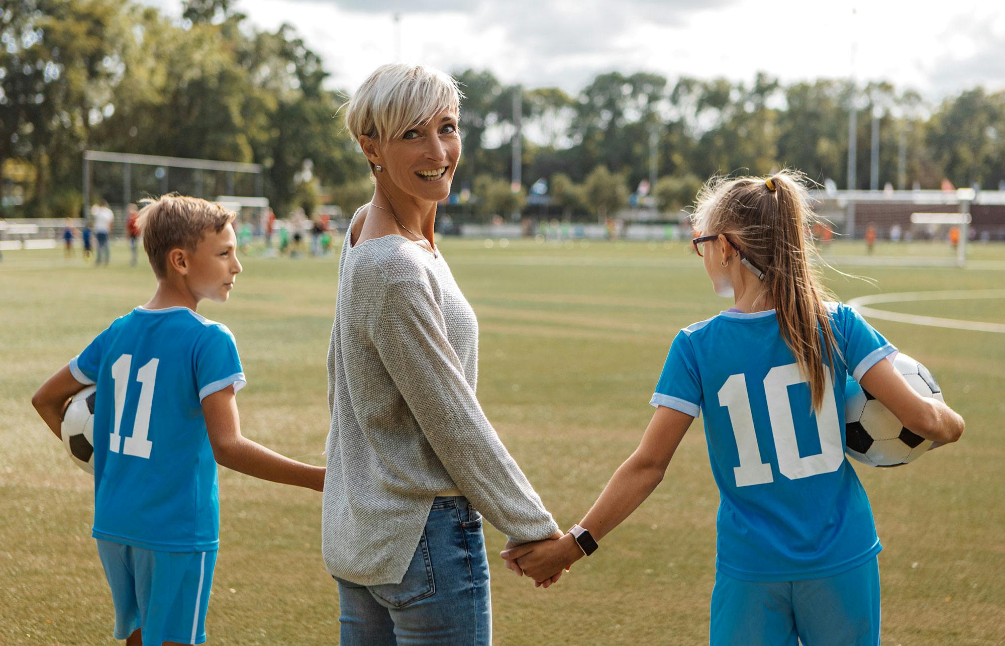En mamma står vid sidlinjen på en fotbollsplan medan hennes barn tränar fotboll.