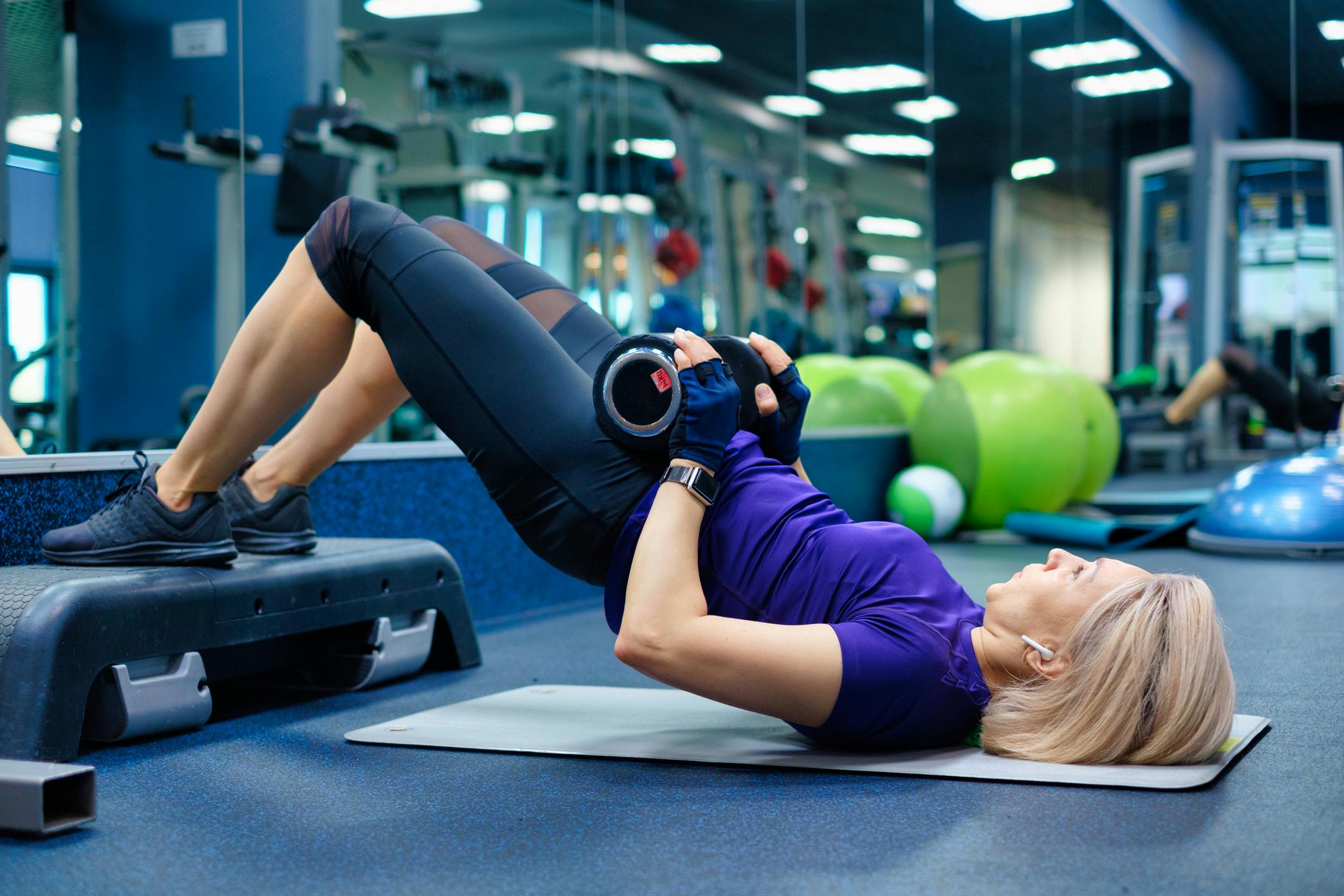 Kvinna i lila träningskläder gör hip thrust på gym