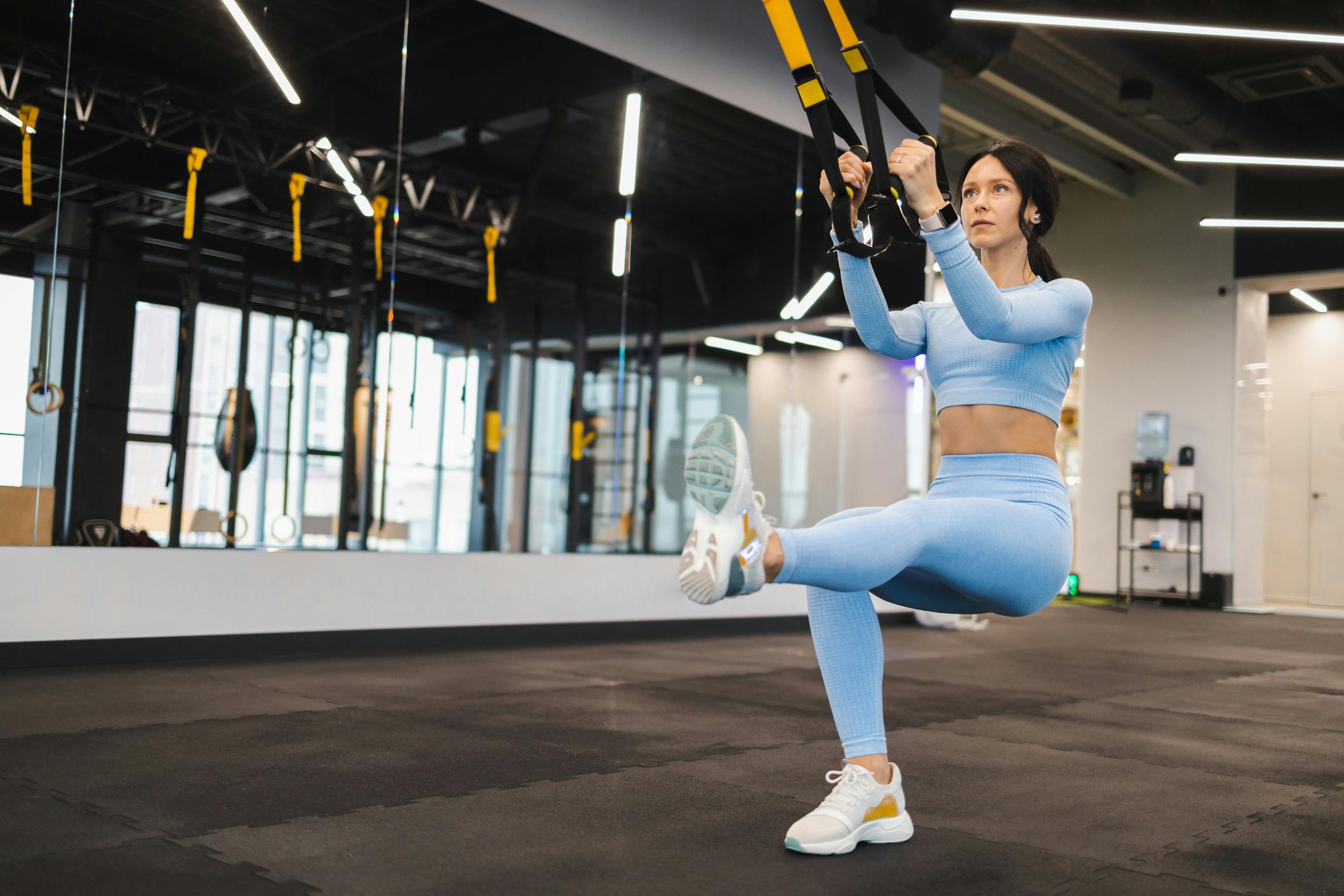 Atletisk kvinde træner ben med 1-bens-squat, som TRX-øvelse