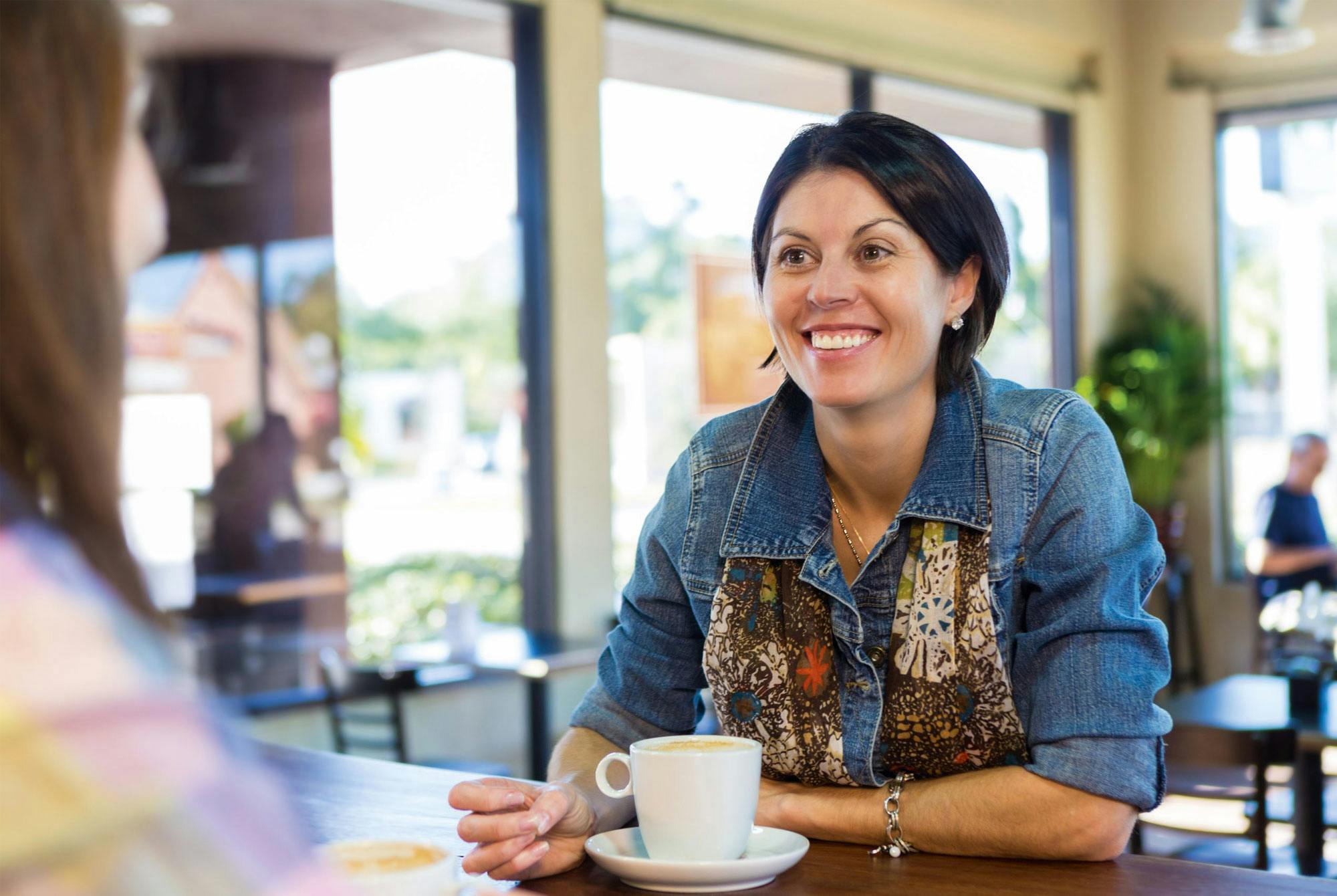 Kvinde sidder på cafe med veninde på trods af smerter