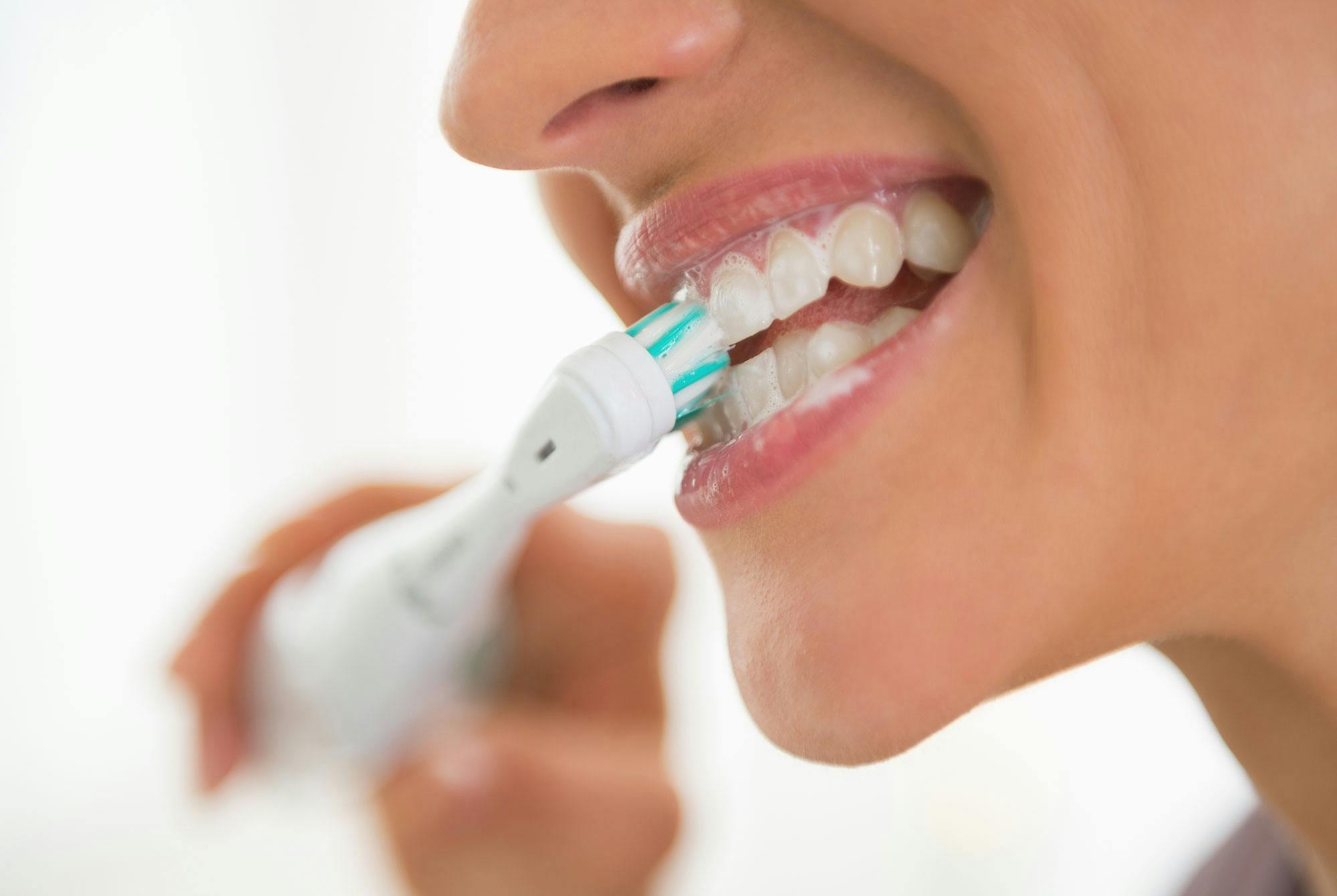 En kvinde børster tænder med en eltandbørste.