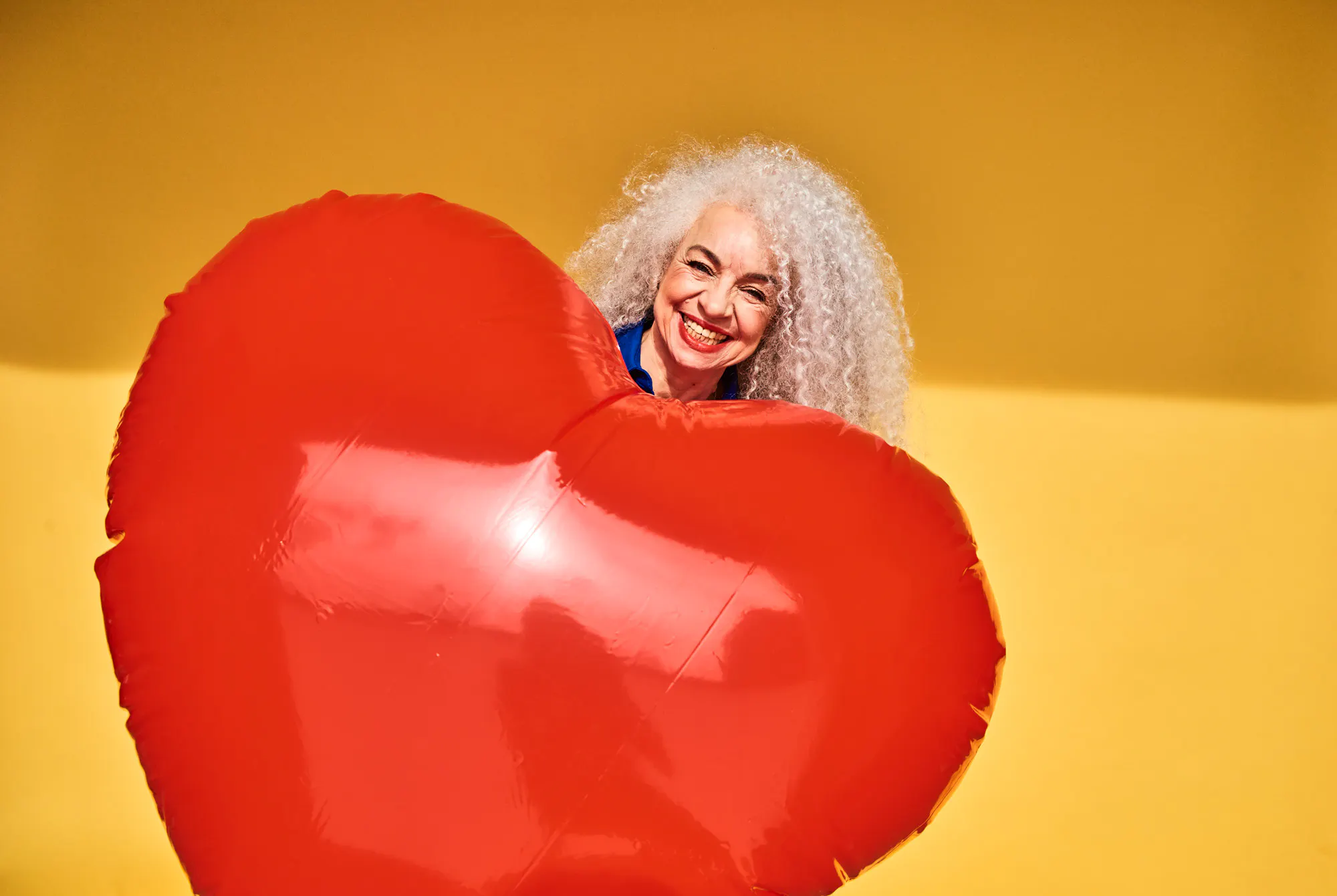 Eldre, glad kvinne holder et stort rødt hjerte