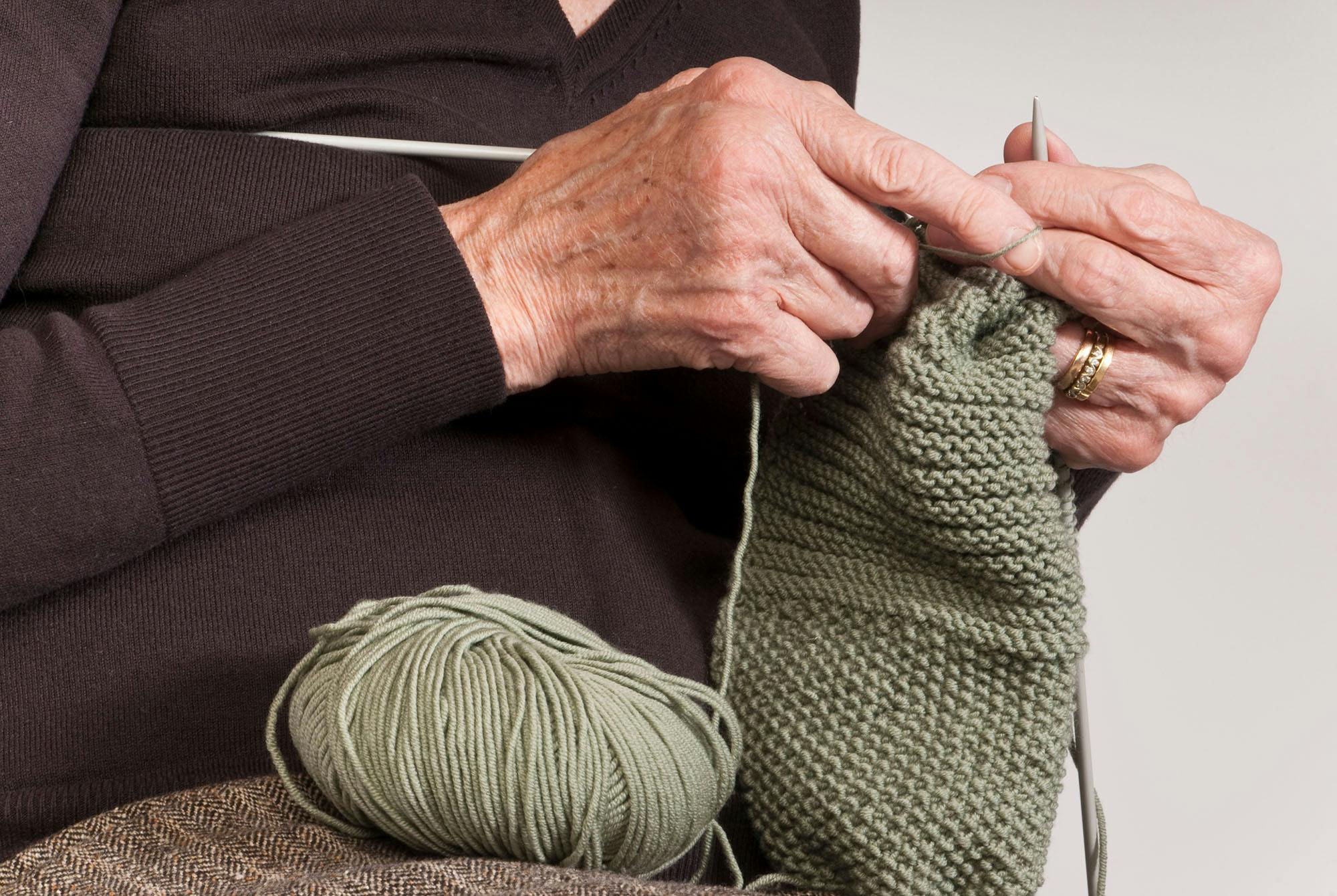 Close up af ældre kvindes hænder, der strikker.