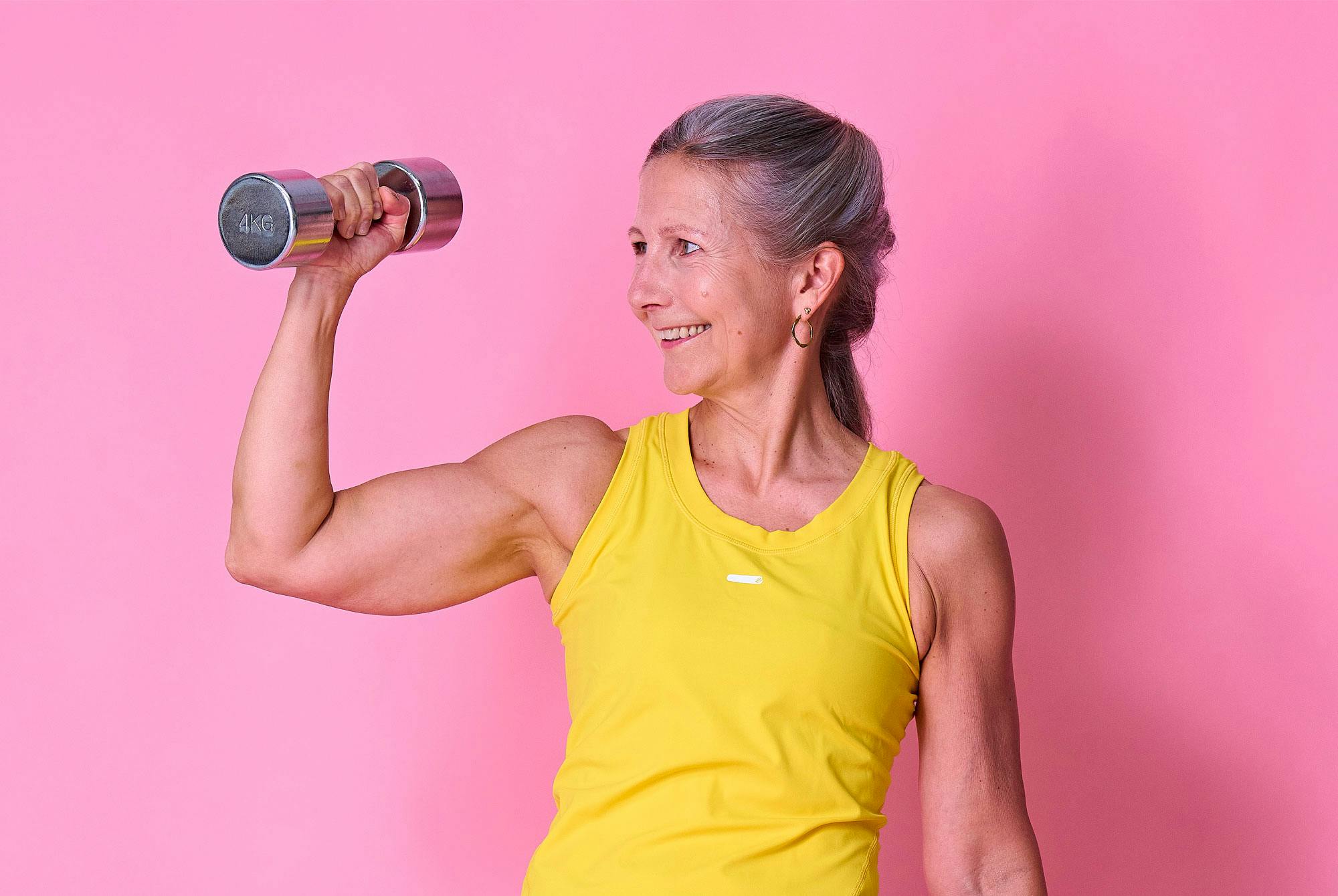 Nainen nostaa käsipainoa ja näyttää lihaksiaan.