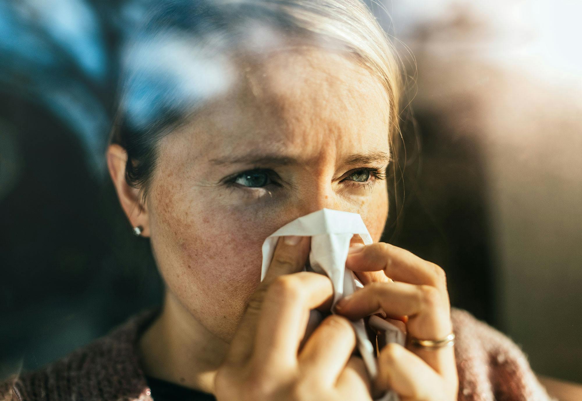 Kvinne som står utenfor og blåser nesen.