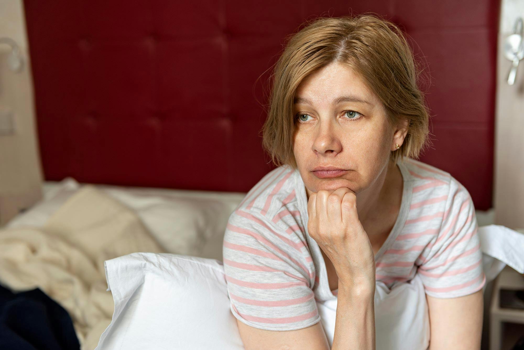 Keski-ikäinen nainen istuu sängyllä huolestuneen näköisenä. Hänellä on perimenopaussi