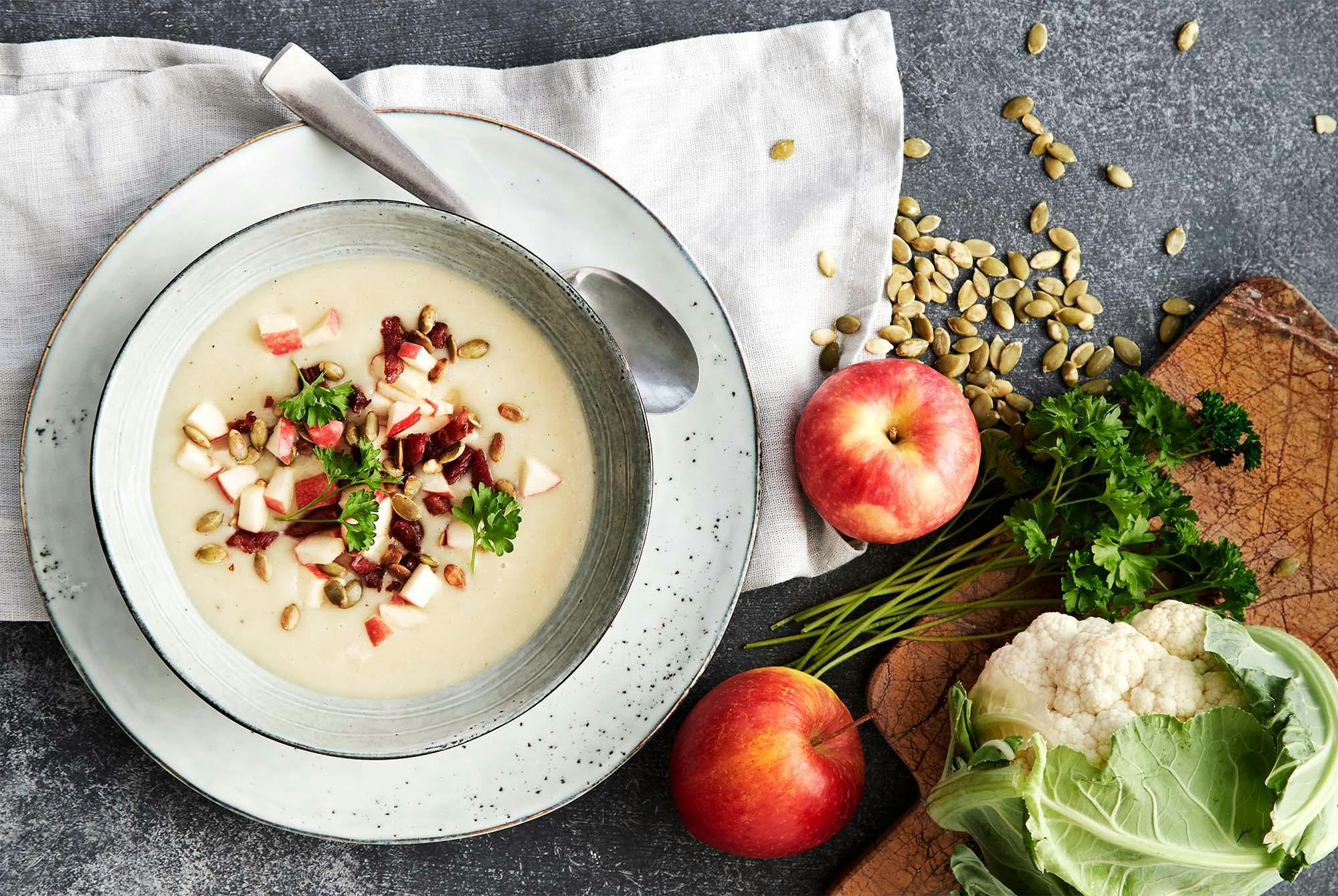 En tallerken potet- og purresuppe med topping av bacon, epleterninger og gresskarkjerner
