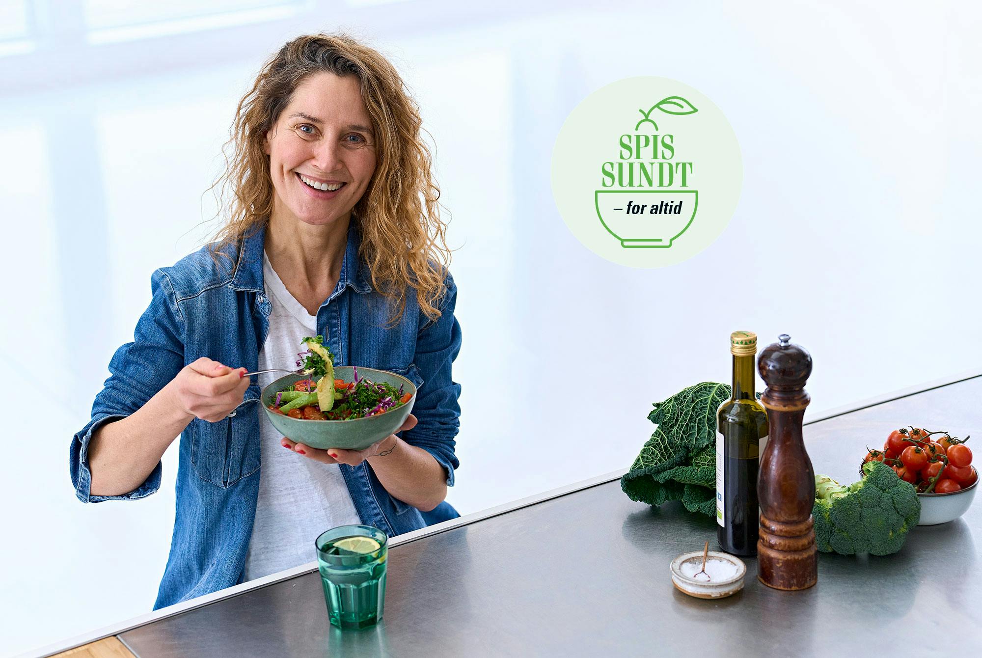 Glad kvinde spiser en skål salat ved et bord