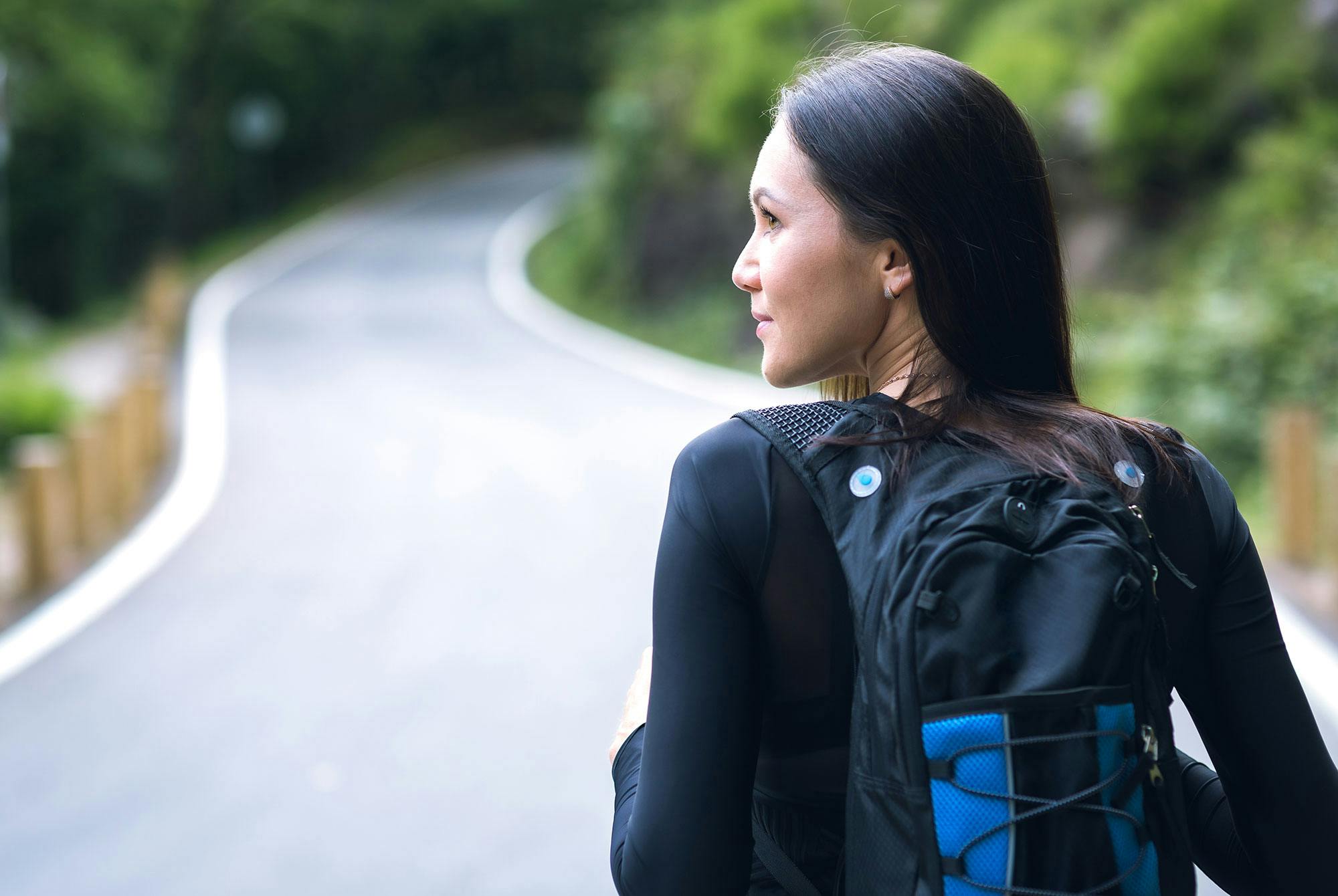 Kvinna som går i japansk stil längs en väg med en ryggsäck på ryggen.