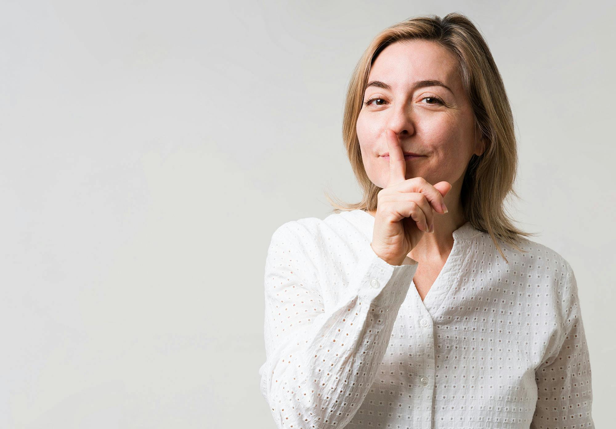 Nainen laittaa etusormensa suulleen. Hän haluaa välttää riitaa kumppaninsa kanssa.