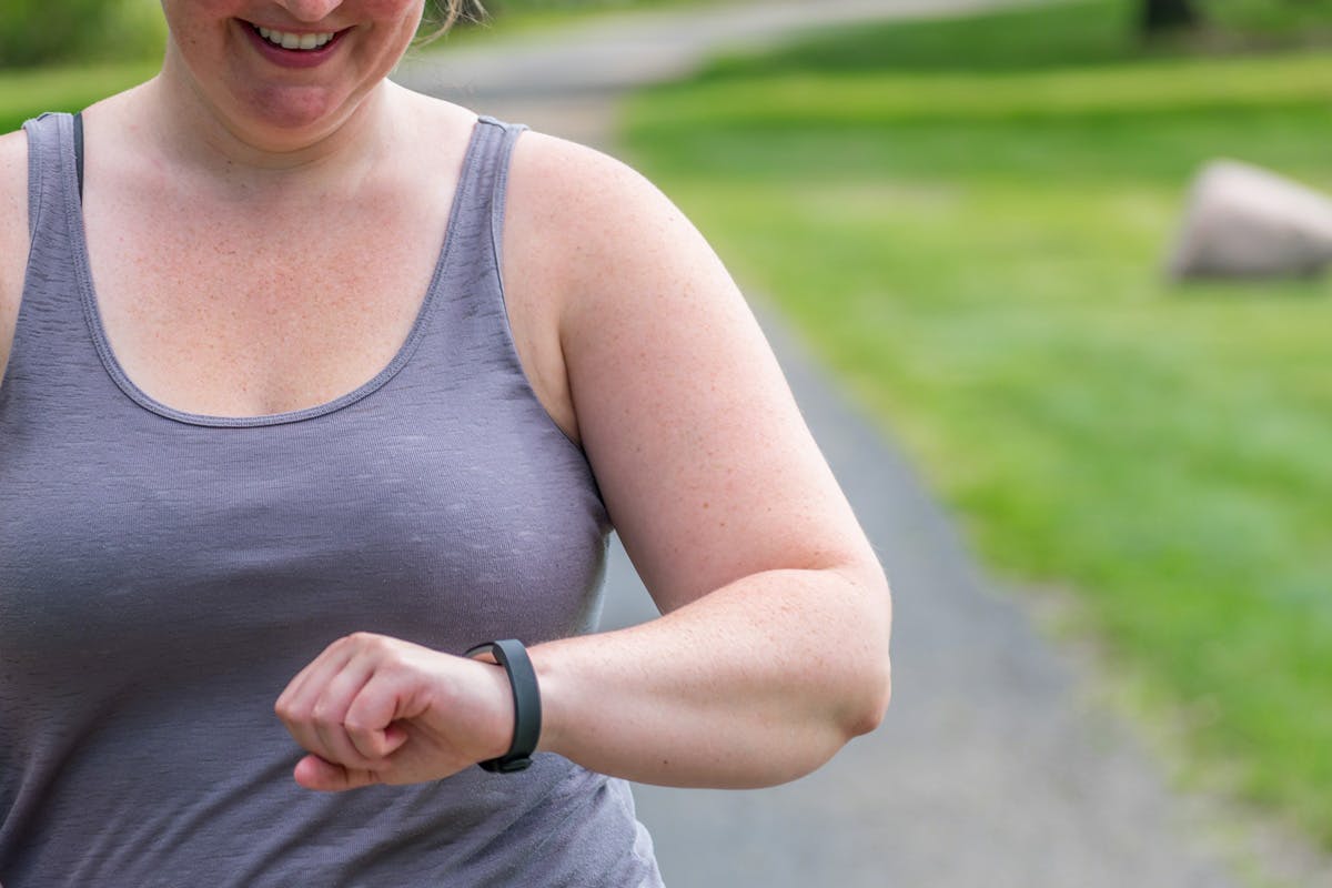 Nainen katsoo kävelylenkillä aktiivisuusrannekettaan – hän kerryttää askelia KUNTO PLUSsan laihdutusta tukevan treeniohjelman mukaisesti.