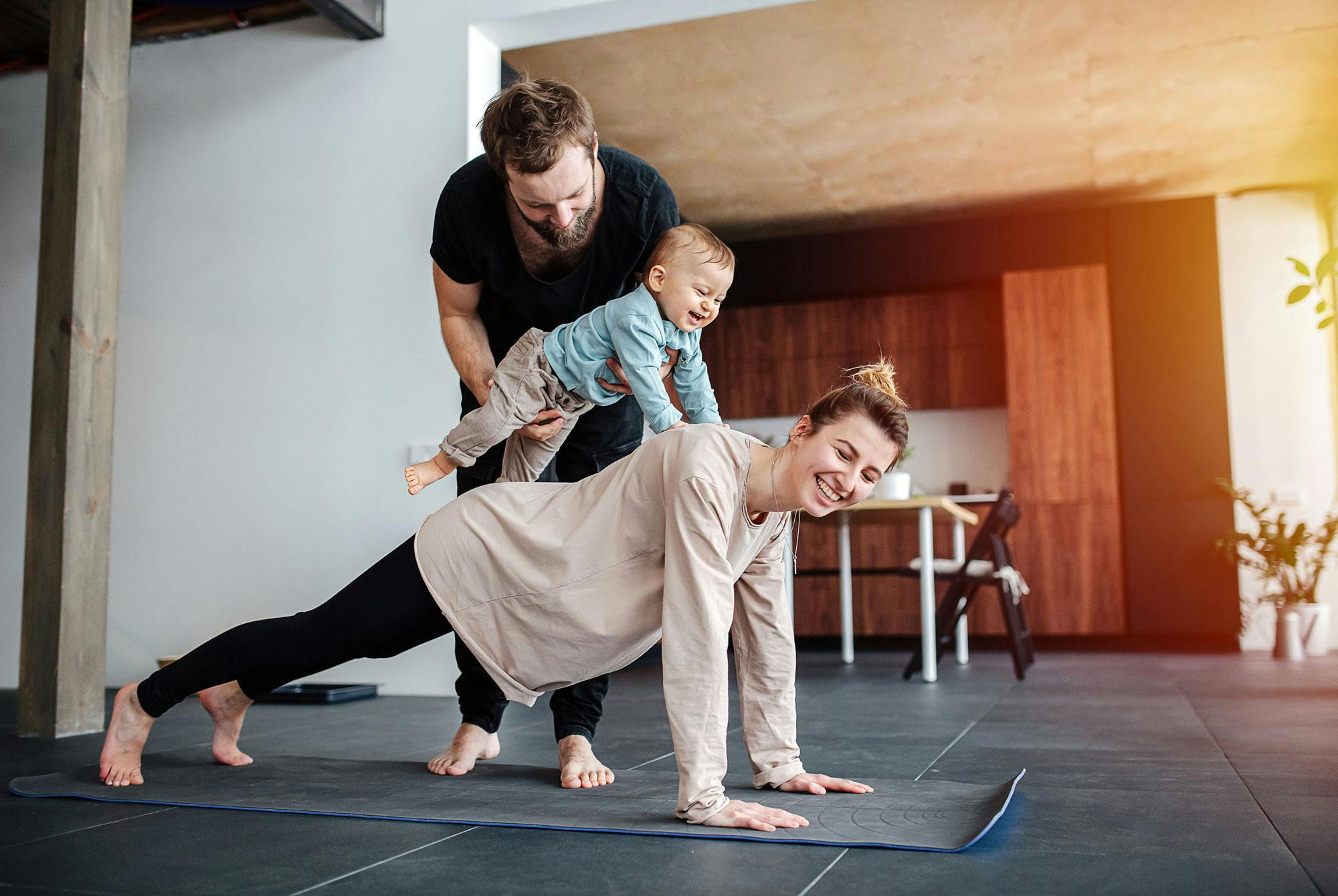 Kvinne ligger i planke med baby på toppen