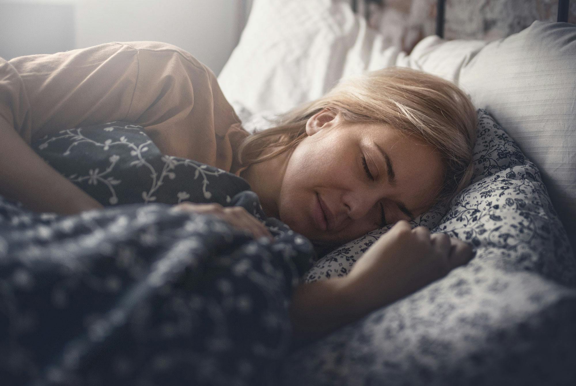 Kvinne sover på høyre side i en seng.