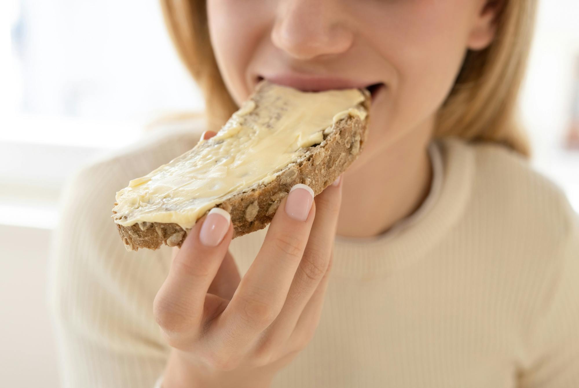 Kvinne spiser et stykke brød med smør