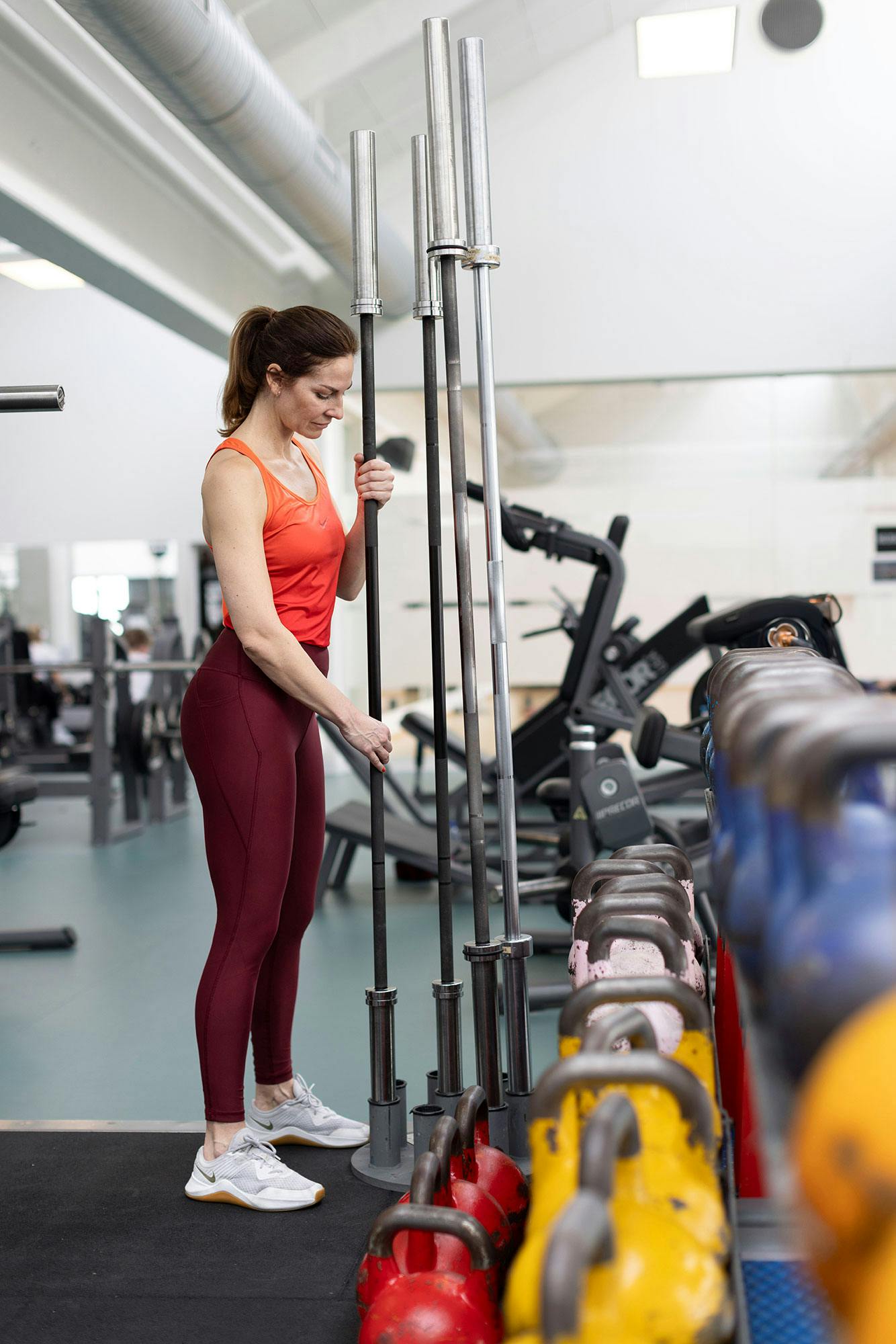 Kvinne på treningssenter setter vektstenger på plass i holder