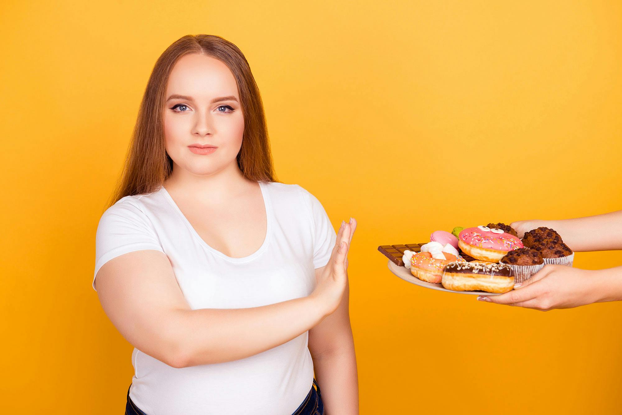 Käsi kurottaa leivonnaista. Nainen haluaa muuttaa yhden ruokailuun liittyvän tottumuksen ja laihtua.