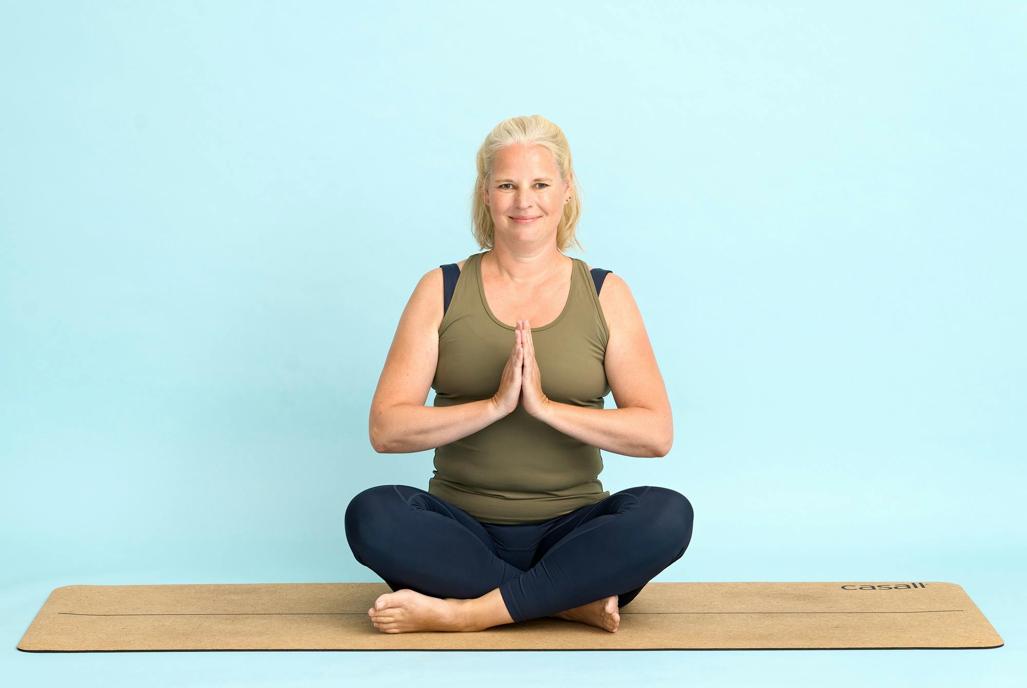 Kvinne sitter i yogastilling på en yogamatte på gulvet.