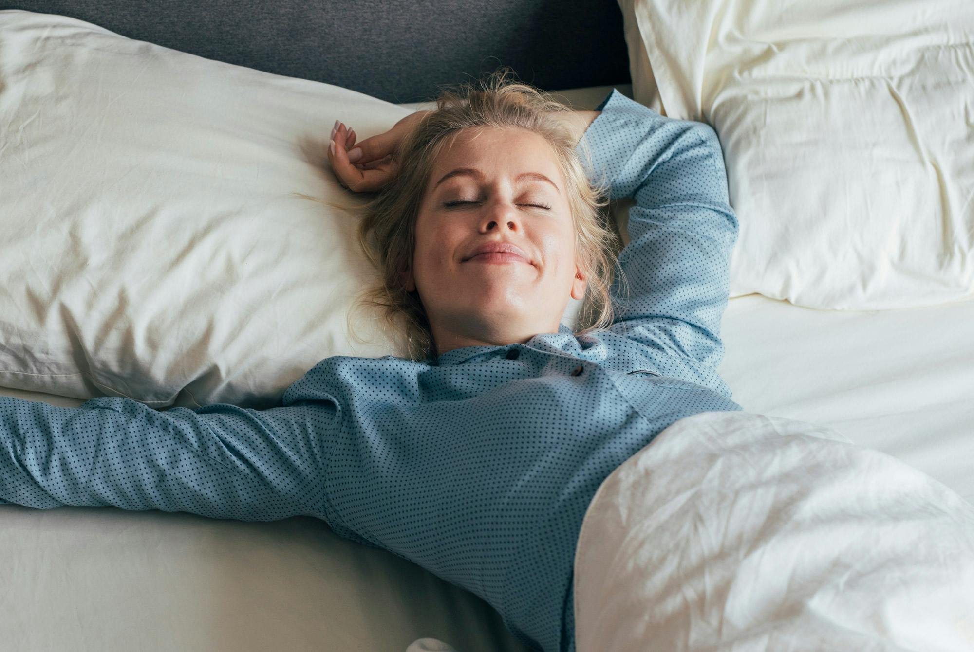 Kvinne ligger i sengen og smiler etter å ha våknet opp test