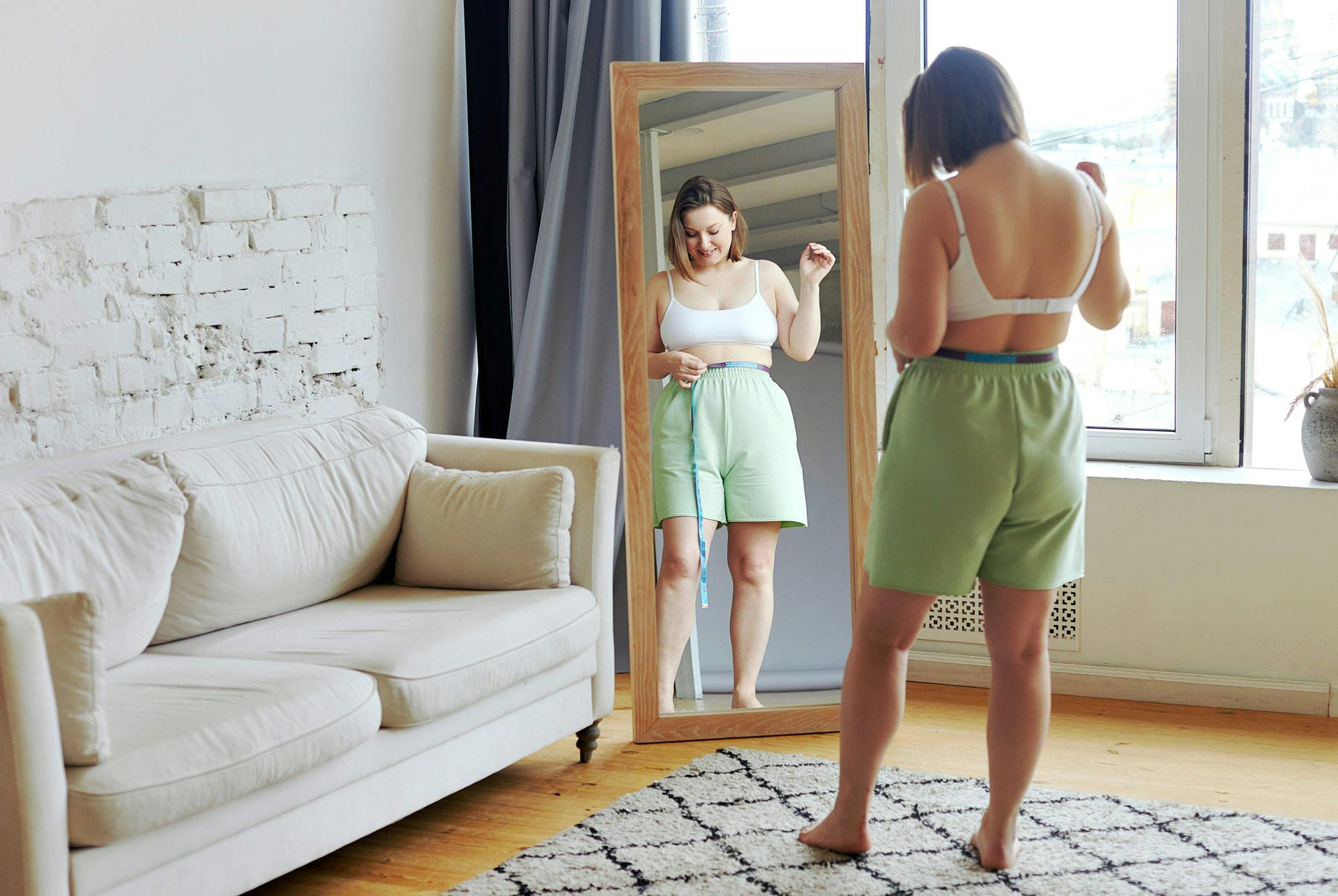 Kvinna framför en spegel mäter sitt midjemått - ett bra komplement till BMI