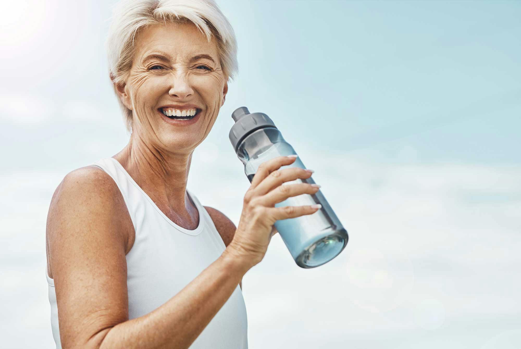 smilende, moden kvinde drikker vand af flaske