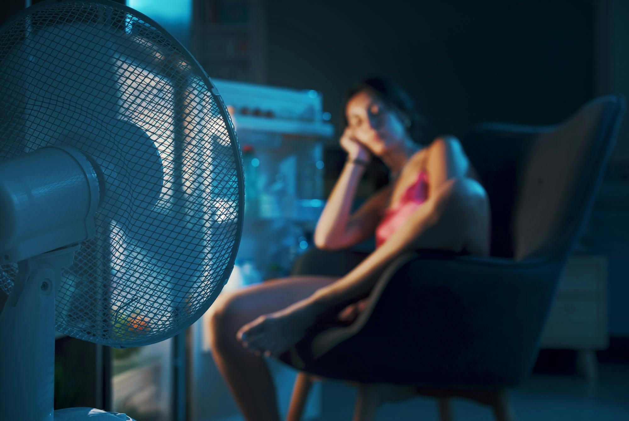 Kvinna med nattliga svettningar sitter framför kylskåpet på natten