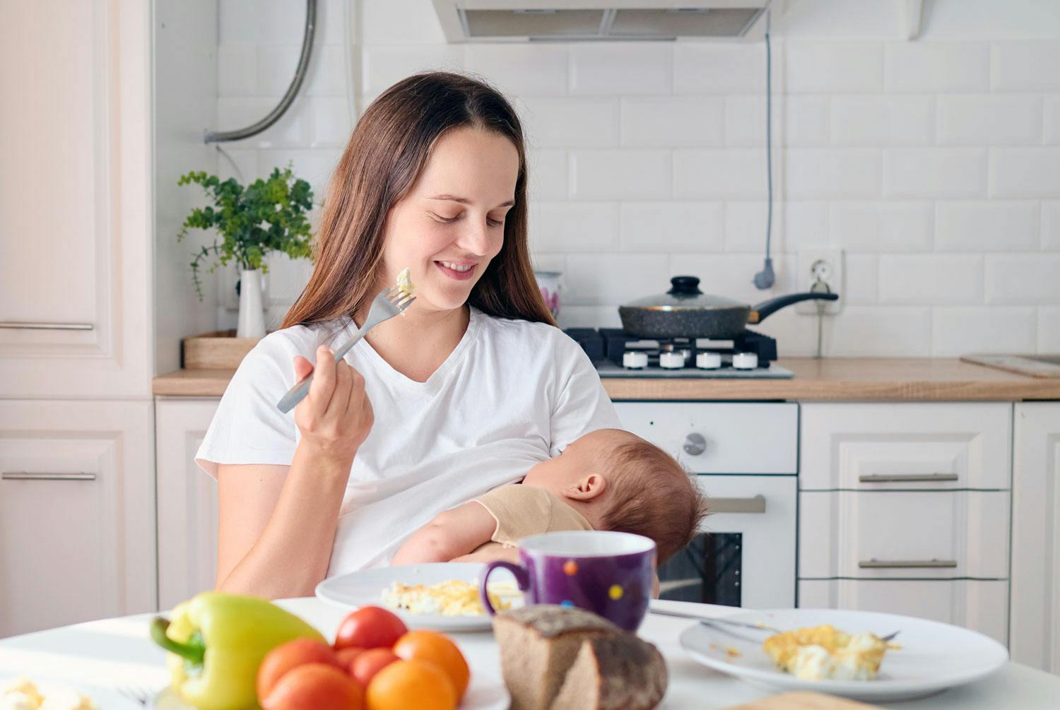 Kvinde ammer sin baby og spiser samtidig. At producere modermælk kræver ca. 645 kcal oveni det normale ligevægtsindtag (beregn det med vores kalorieberegner).