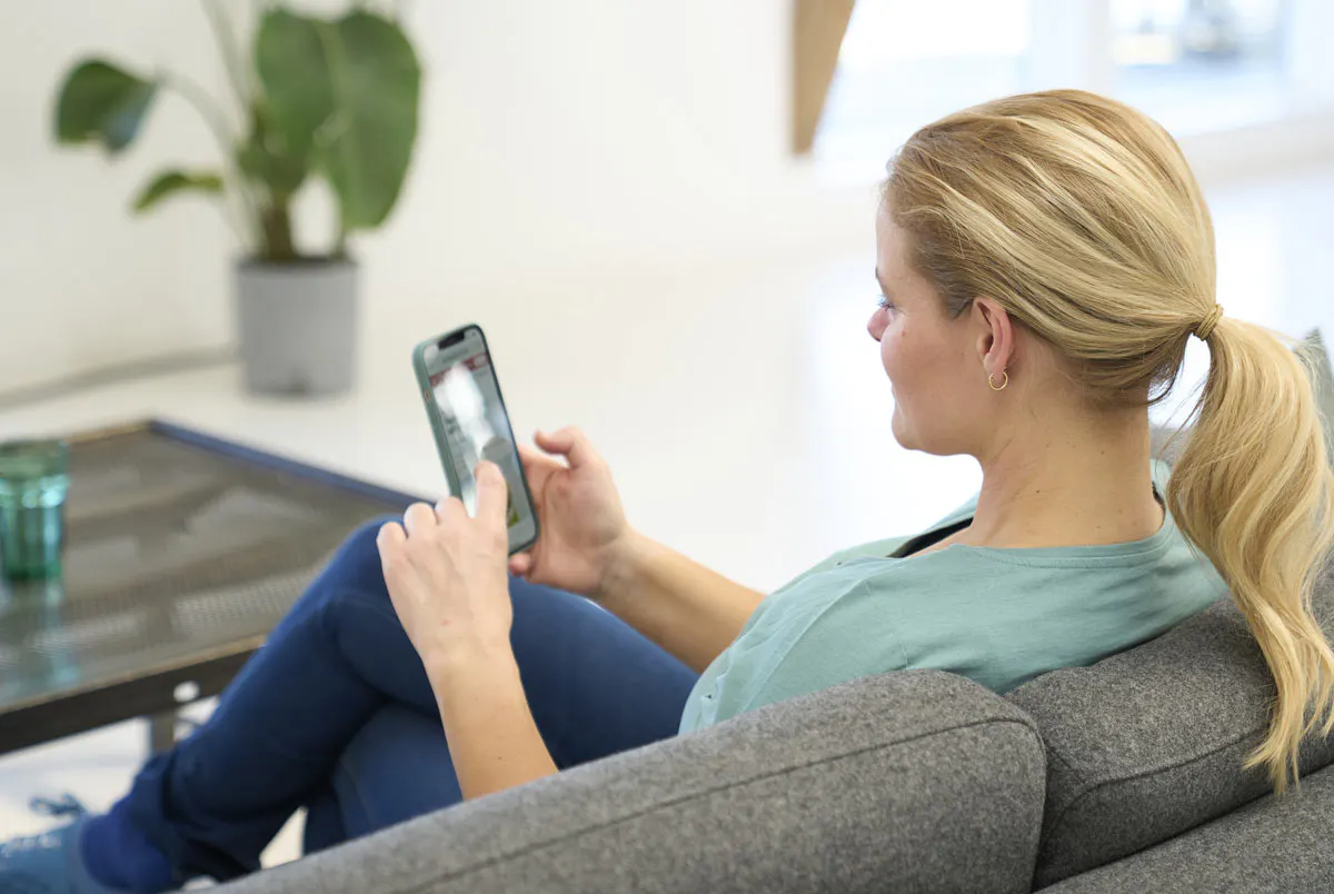 Kvinde sidder med telefon i sofa. Hvor mange kalorier forbrænder man om dagen uden motion?