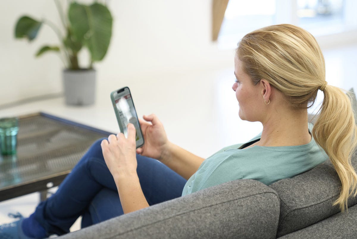 Kvinne sitter med telefon i sofa. Hvor mye forbrenner man på en dag uten trening?