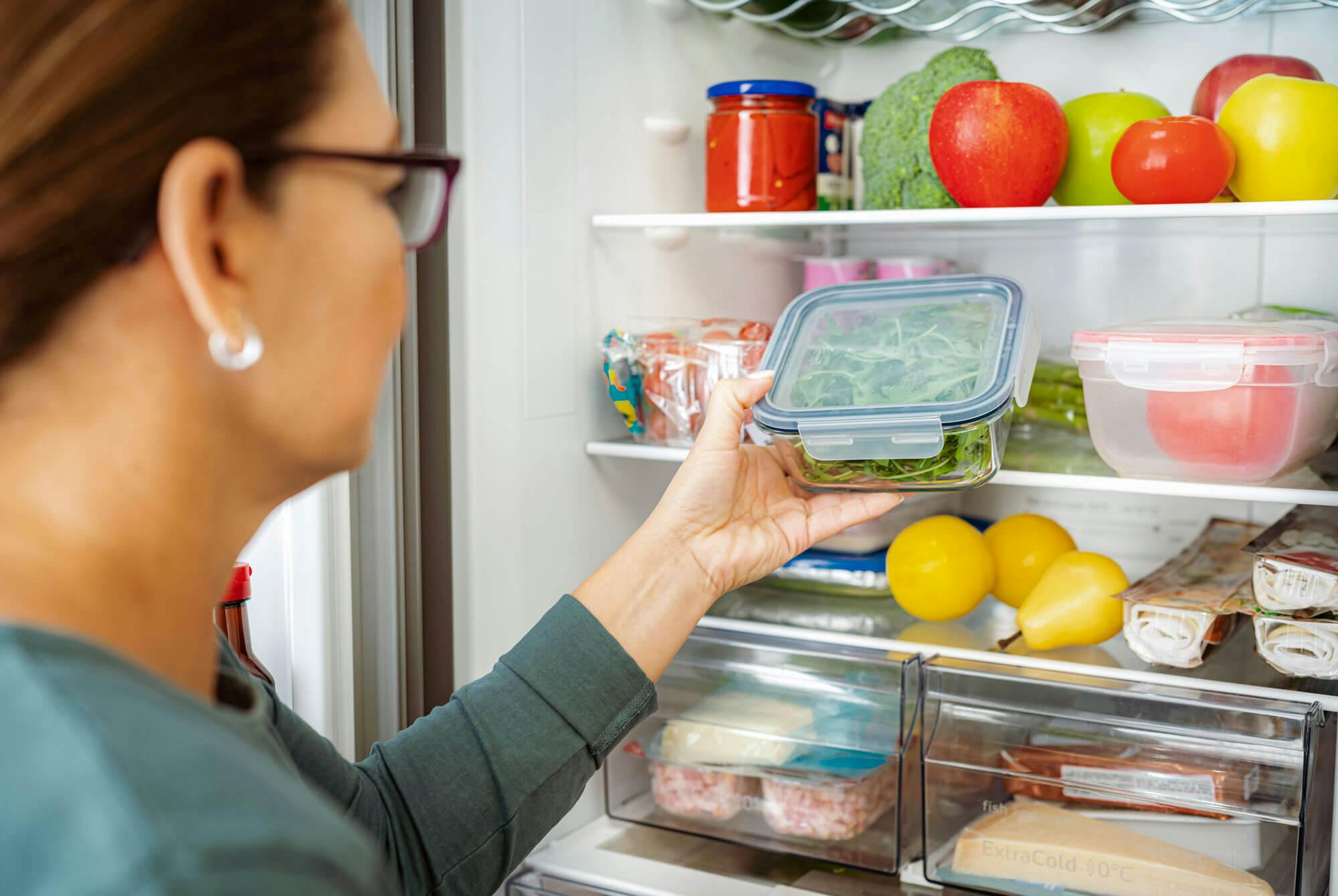 nainen avaa jääkaapin, jossa on ketoruokavalioon sopivia elintarvikkeita