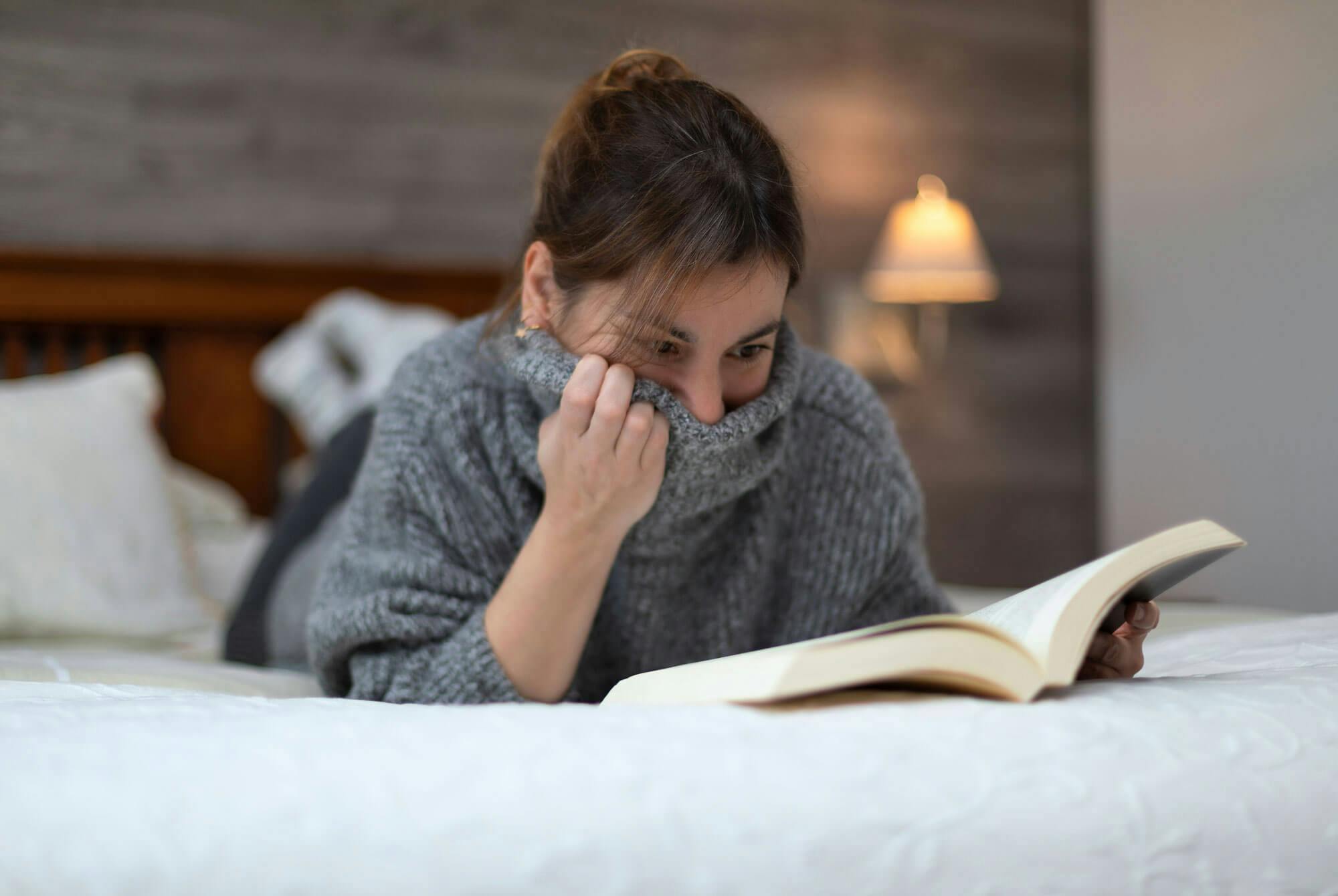 Nainen makaa sängyllä ja lukee pelottavaa kirjaa.