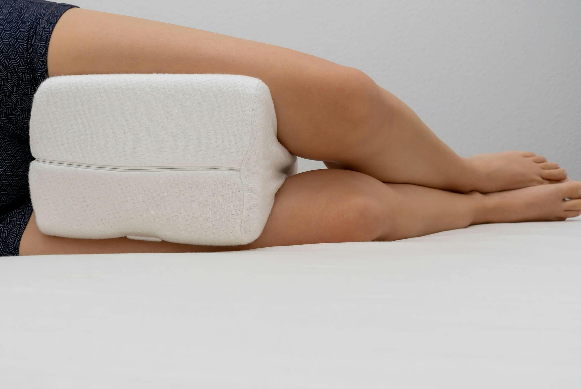 Kvinne med hekseskudd sover med en støttepute mellom beina