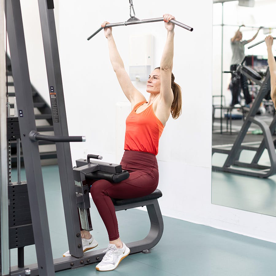 kvinde, der er i gang med at lave lat pulldown – fører stangen kontrolleret op