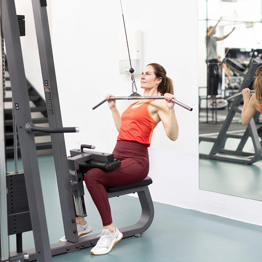 kvinde, der er i gang med at lave lat pulldown – trækker stangen ned