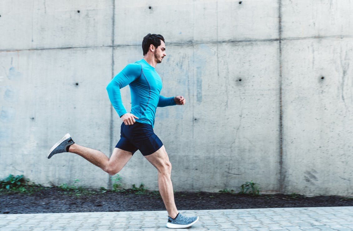 Mannlig løper i blå trøye løper med treningsklokke