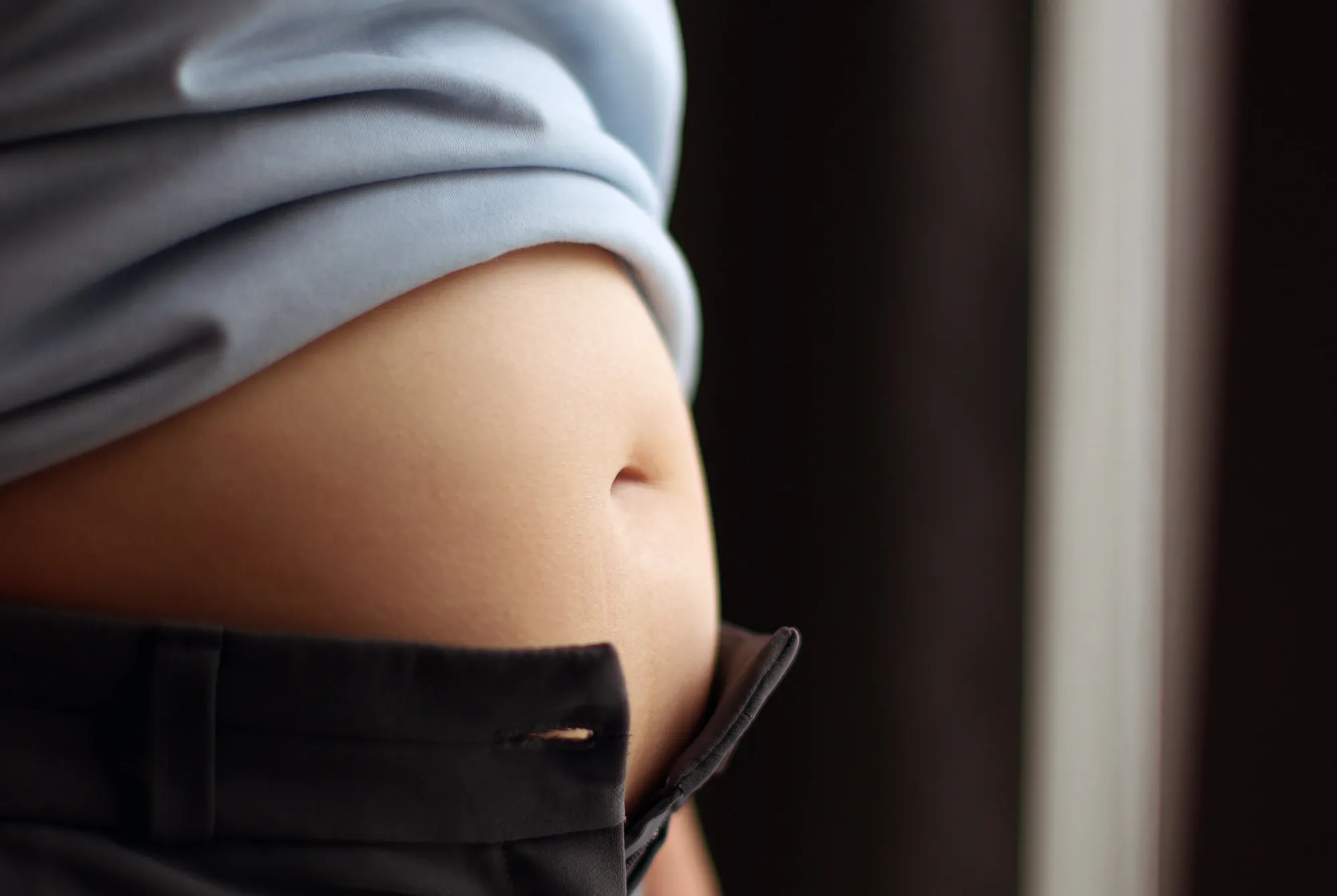 Kvinne med oppblåst mage og luft i magen har kneppet opp buksene.