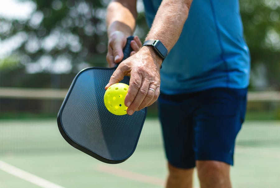 Man som håller en pickleballracket och boll i handen
