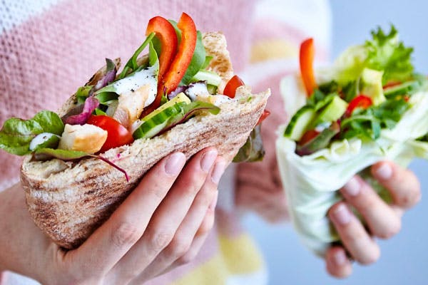 En hånd holder et pitabrød med kylling og salat i