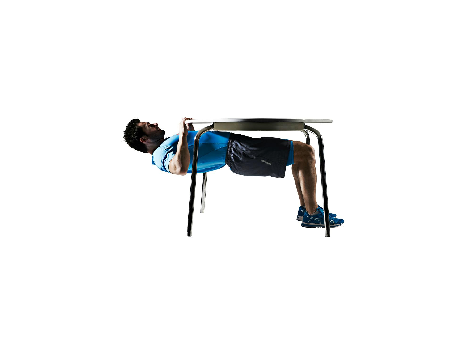 Mann i blå T-skjorte trener pull-ups under bord
