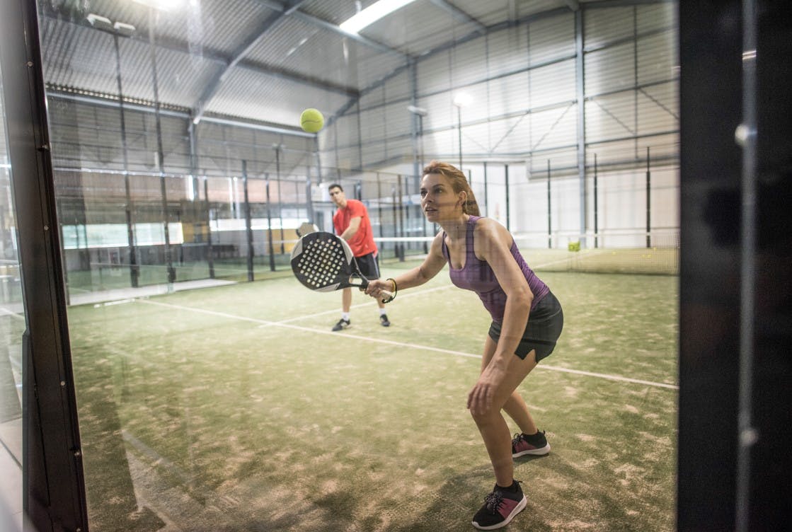 Kvinna spelar padeltennis mot en glasvägg