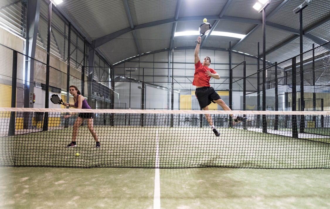 Man och kvinna spelar padel. Man anstränger sig för att nå en boll på en padelbana