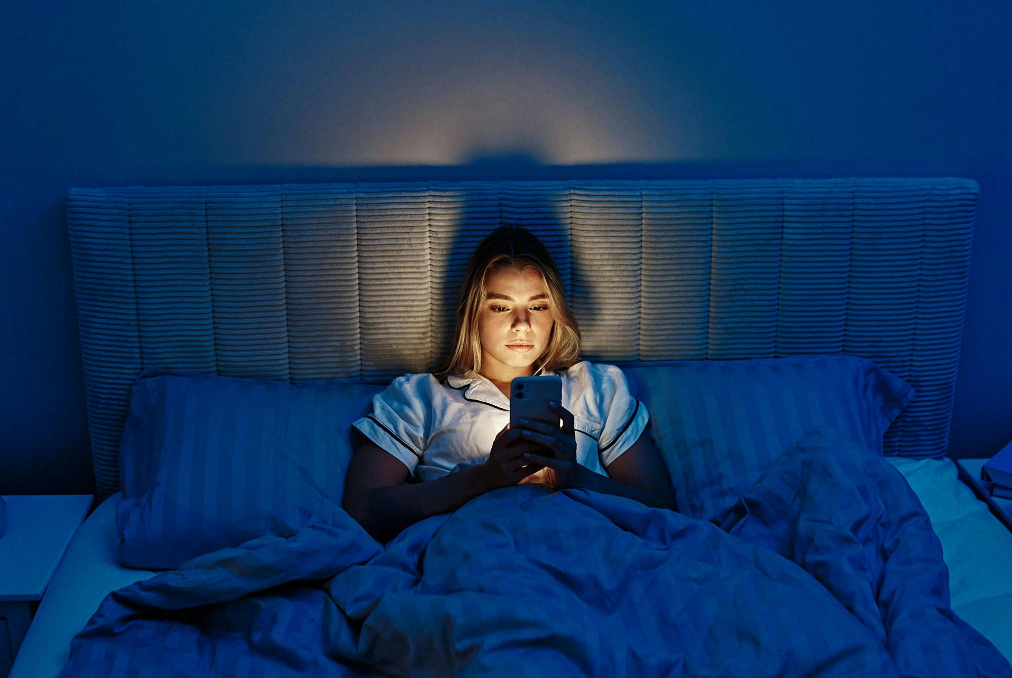 Bedtime procrastination: Kvinde ser på mobilen i sin seng i stedet for at sove.