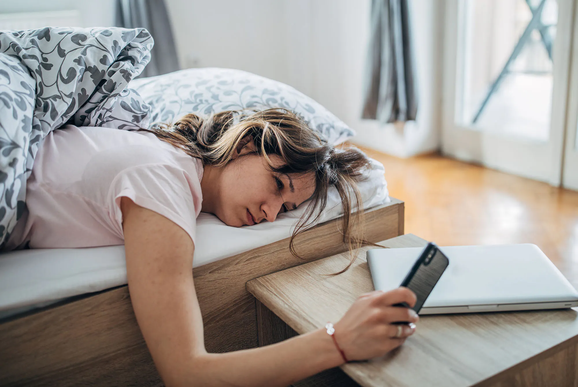 kvinne som ligger i sengen og ser på telefonen sin.