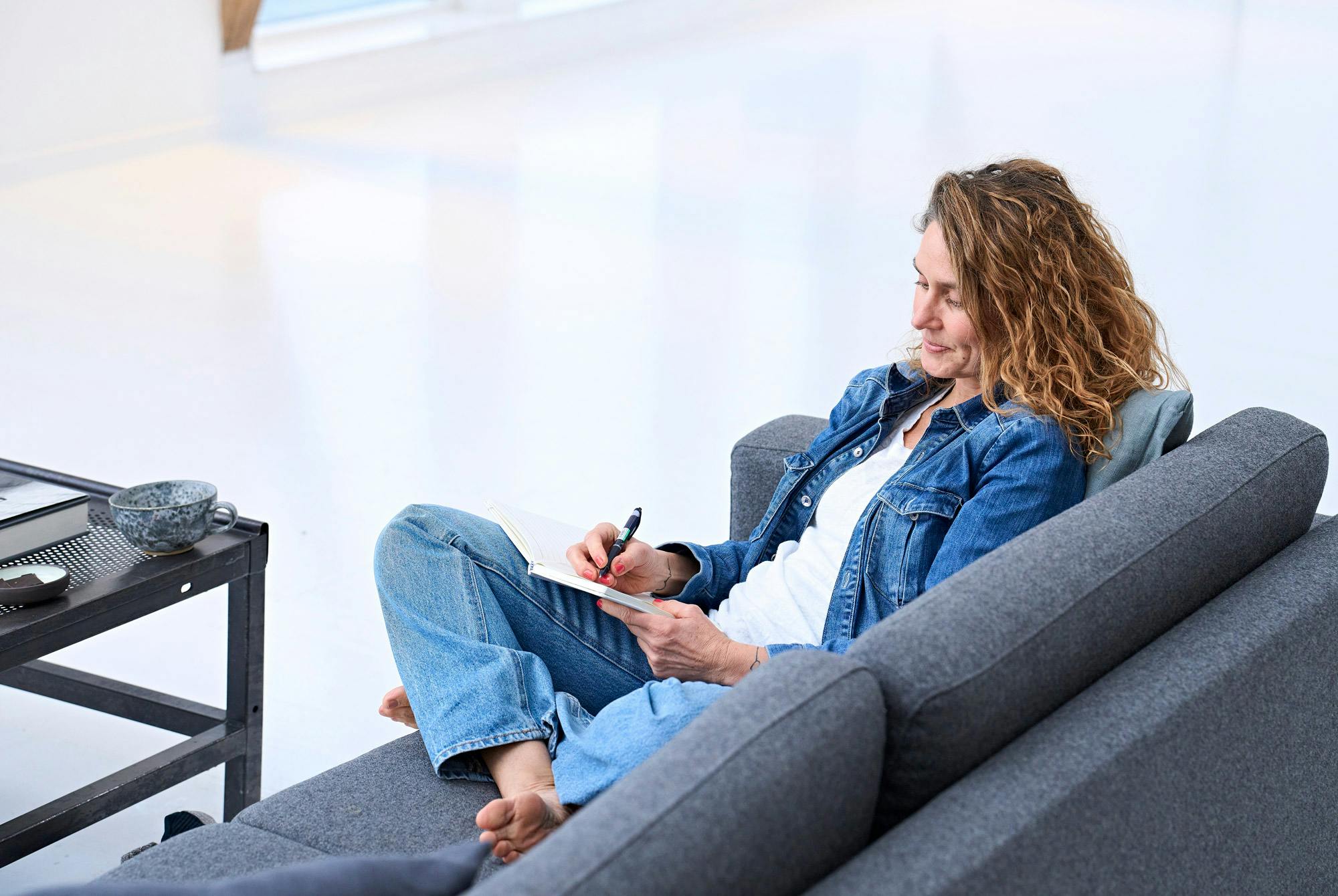 Kvinne som sitter i en sofa og skriver i en notatbok, dagbok