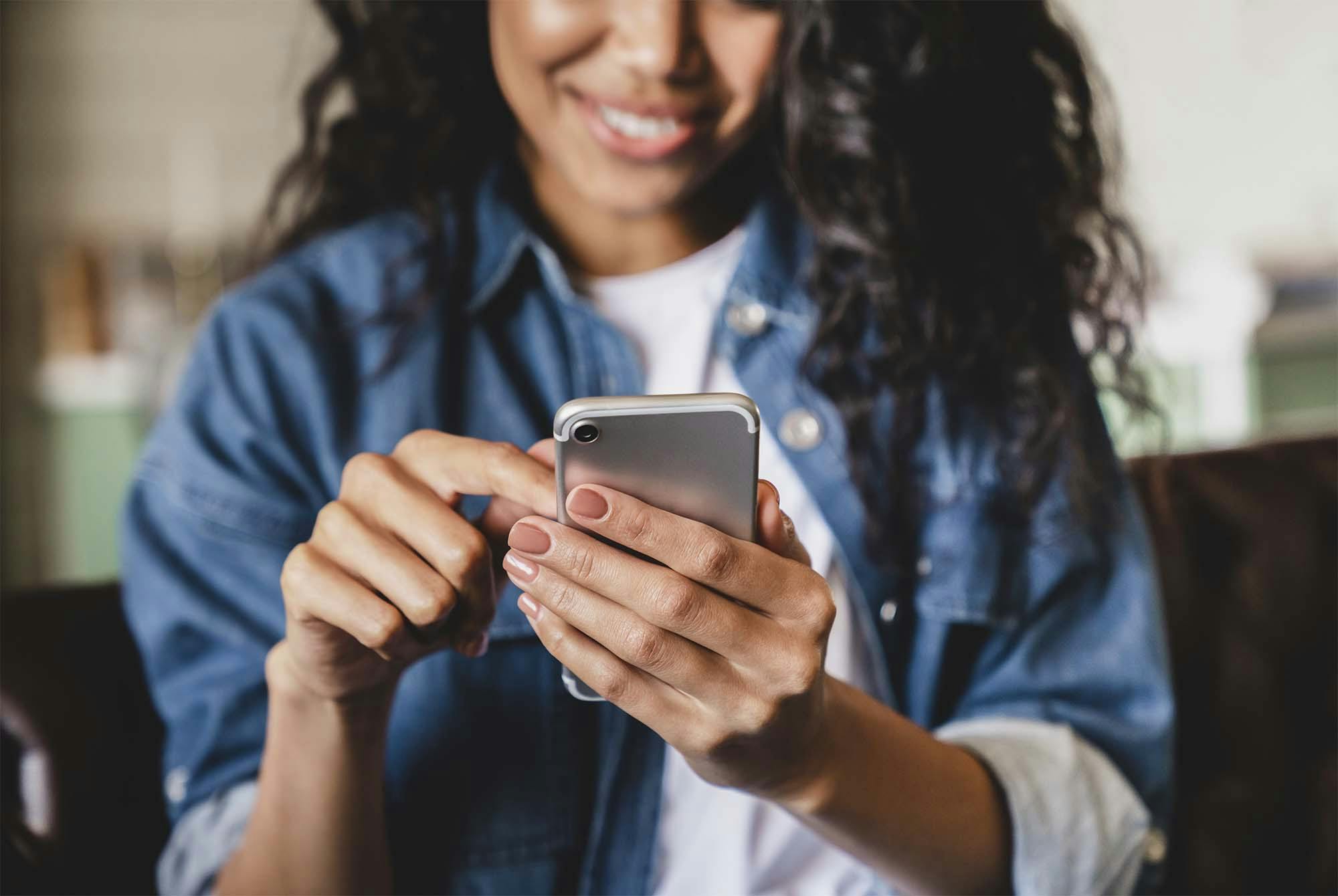 En kvinde sidder sammen med andre, men kigger ned i sin telefon. Hun har et stort forbrug af skærm. Her kan du læse om gode skærmvaner.